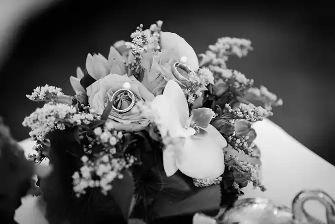 Onelovephoto Ein Schwarz-Weiß-Foto eines Straußes mit Rosen, Orchideen und kleinen Blumen, geschmückt mit zwei Eheringen, die auf den Blütenblättern ruhen. Hochzeitsfotografie in Mannheim und Heidelberg