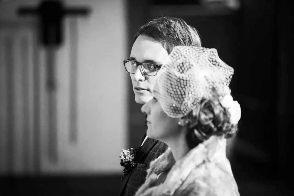 Onelovephoto Ein Schwarz-Weiß-Foto eines Mannes mit Brille und einer Frau mit einem alten Netzfascinator, beide förmlich gekleidet, die nebeneinander stehen und nach vorne schauen. Hochzeitsfotografie in Mannheim und Heidelberg