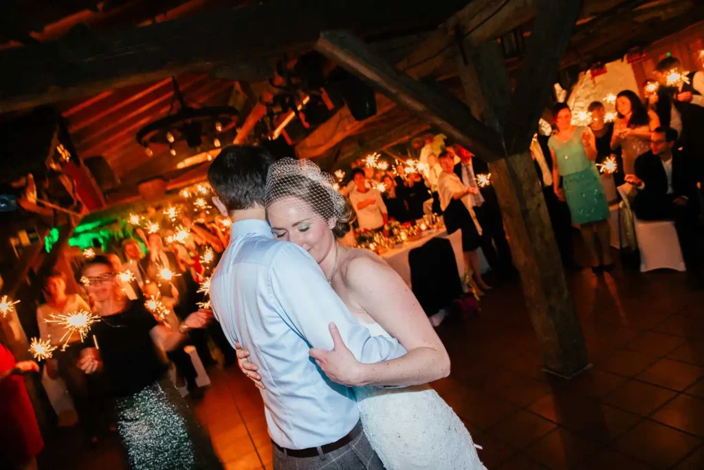 Als Hochzeitsfotograf in Ladenburg halte ich den Moment fest, wenn das Brautpaar einen langsamen Tanz teilt, während Gäste mit Wunderkerzen in einer warm beleuchteten, rustikalen Location mit Holzbalken feiern. Onelovephoto - Hochzeitsfotografie in Mannheim und Heidelberg