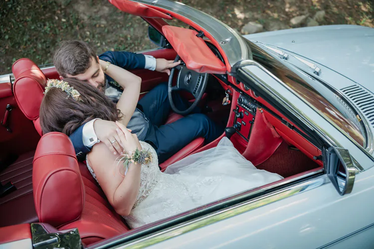 Onelovephoto Ein frisch verheiratetes Paar in Hochzeitskleidung sitzt in einem weißen Cabrio mit rotem Interieur. Sie umarmen sich und sind einander zugewandt, von oben aufgenommen, und genießen einen freudigen, intimen Moment. Hochzeitsfotografie in Mannheim und Heidelberg