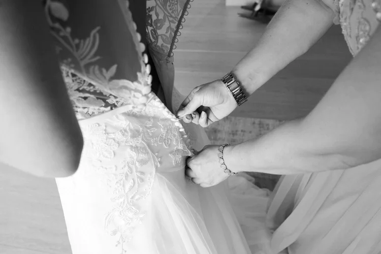 Onelovephoto Ein Schwarz-Weiß-Foto in Nahaufnahme von jemandem, der die Knöpfe am Rücken des Spitzenhochzeitskleides einer Braut befestigt. Hochzeitsfotografie in Mannheim und Heidelberg